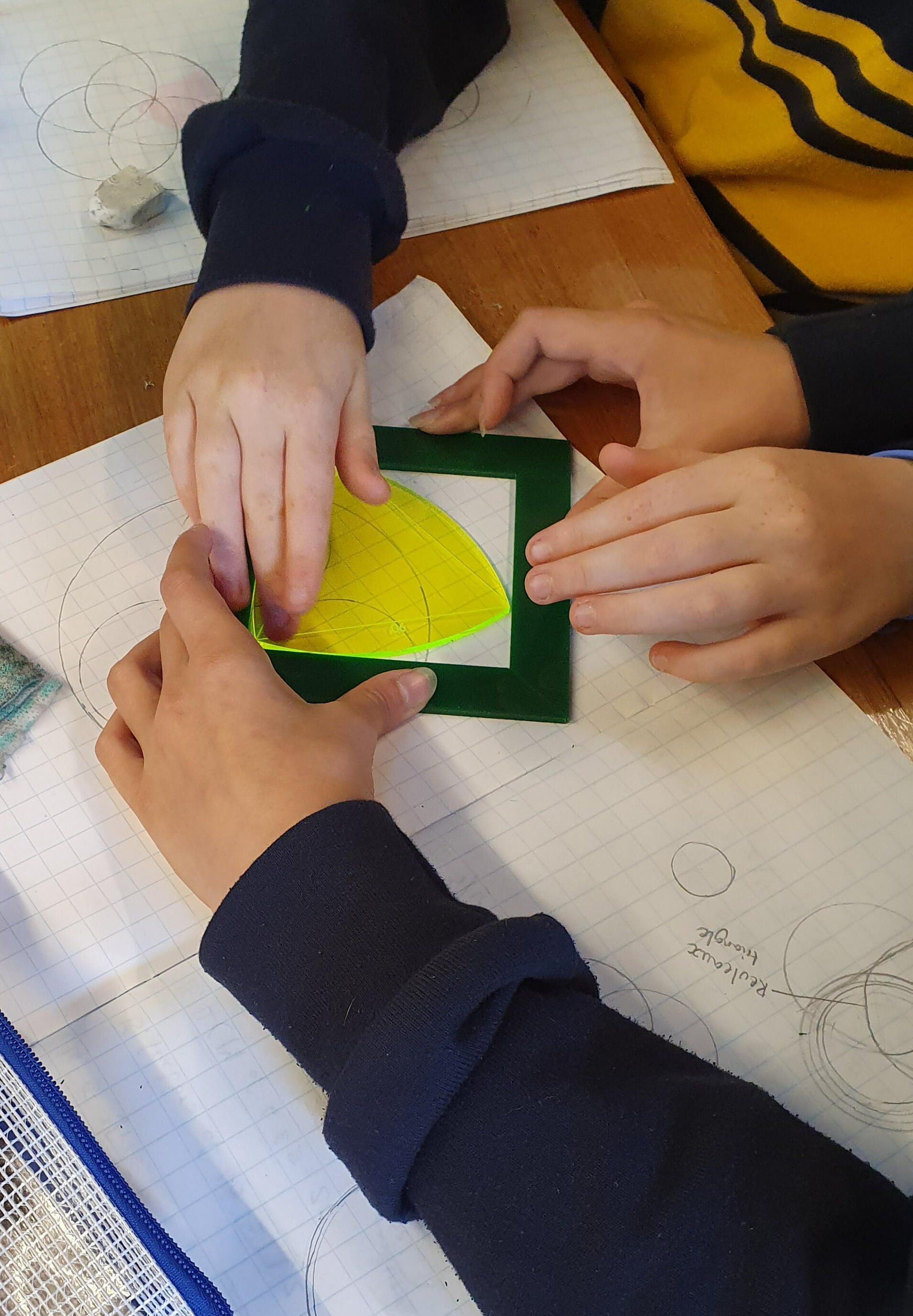 Students collaborating on a Reuleaux triangle investigation, testing a yellow cut-out shape of constant width against a square frame